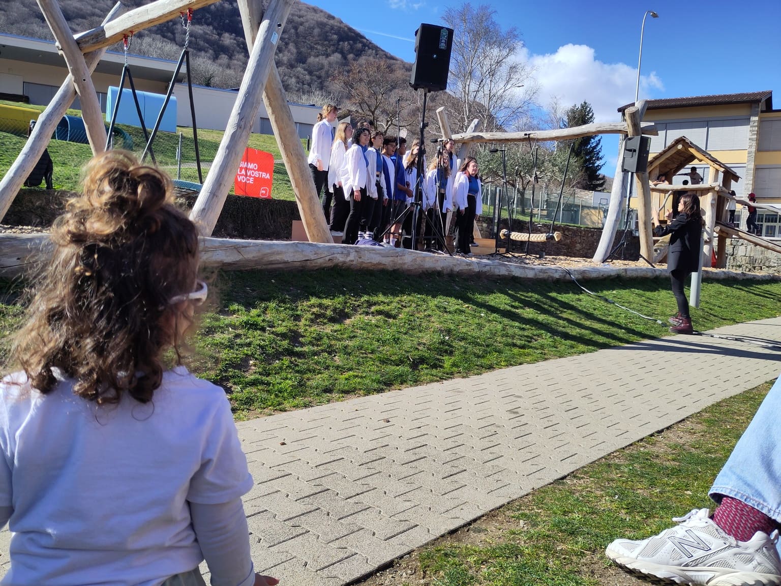 Il MixTape Pop Choir (MAT) canta con passione, rappresentando la voce e l'energia dei giovani. Una bambina in primo piano li sta ascoltando.
